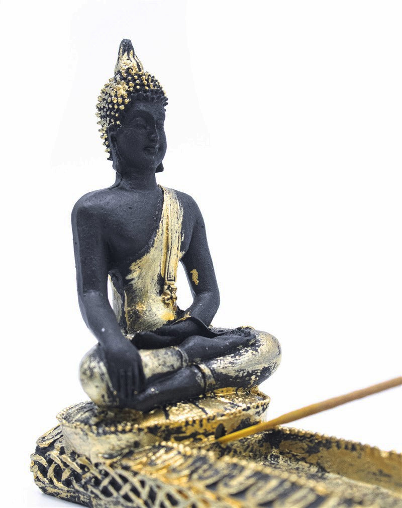A seated Buddha figurine in a dark charcoal black finish with metallic gold accents, shown on a white background with a gold tray and incense stick.