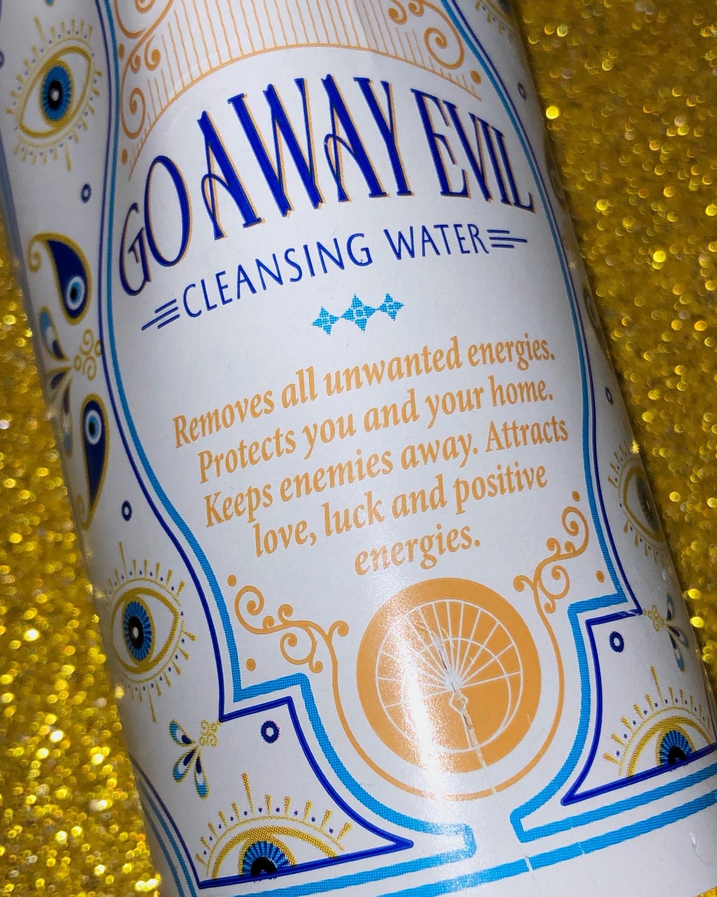 Bottle labeled 'Go Away Evil Cleansing Water' with decorative design on a glittery yellow background